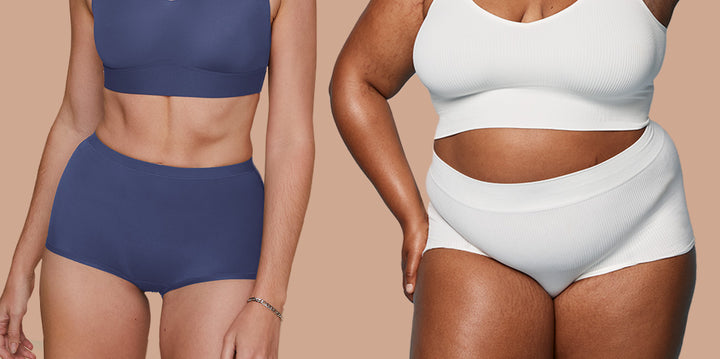 Two models standing side by side against a tan backdrop. The model on the left is wearing the Bliss Boyshort in Twilight and the model on the right is wearing the Lounge Ribbed Boyshort in White.