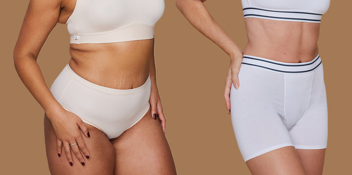 Two models standing side by side against a tan background. The model on the left is wearing the Bliss Highwaist Brief in Black and the model on the right is wearing the Cloud Cotton Bikini in Indigo.