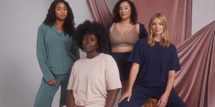 Four models dressed in Harper Wilde Perfect Pima Pajama sets in various colors - Rainforest green, Bellini pink and Navy. They pose seated and standing against a pink draped background.